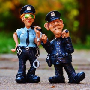 Two playful police figurines, complete with handcuffs and batons, depicted in a comical outdoor setting.