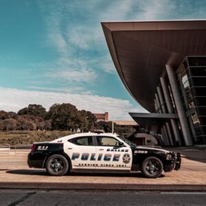 A police car parked outside a modern architectural building during the day with clear blue skies.