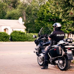 A police officer on a motorbike observes a quiet suburban street lined with greenery.