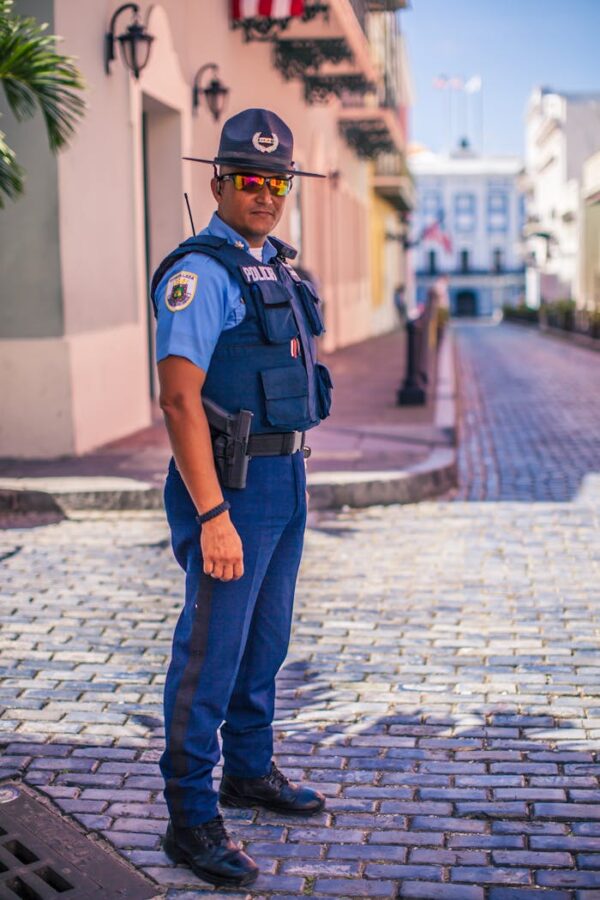Uniformed police officer stands on a cobblestone street, ensuring public safety.