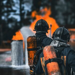 Two firefighters in protective gear facing a large blaze with determination outdoors.