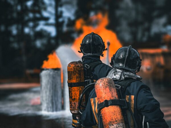 Two firefighters in protective gear facing a large blaze with determination outdoors.